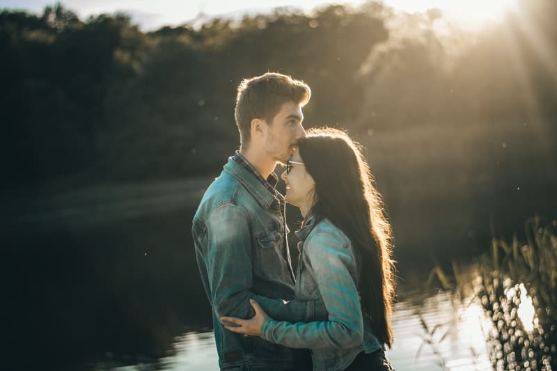 man kissing woman in forehead near lake