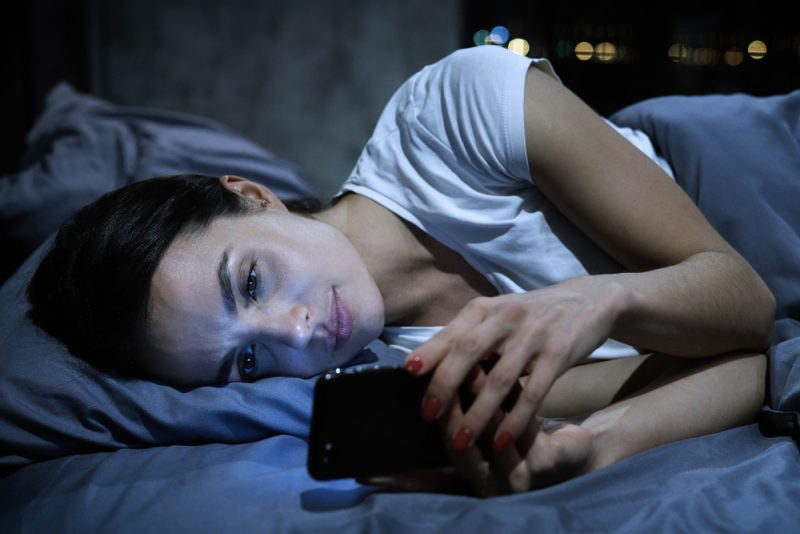 kvinna som ligger i sängen och håller sin telefon