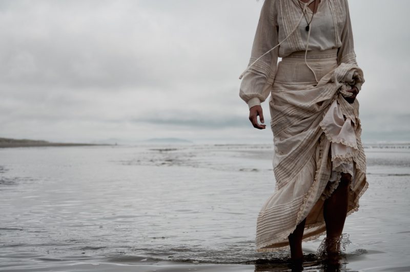 kvinna i lång vit klänning på stranden