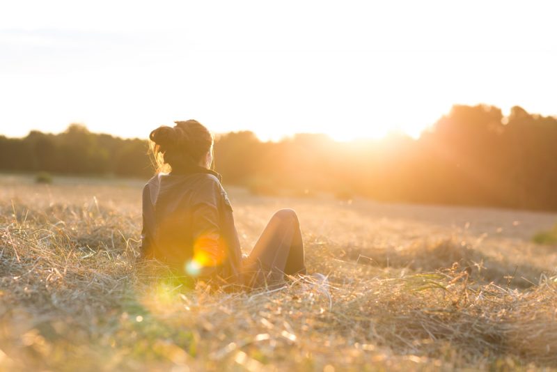 kvinna som sitter på gräset och tittar på solnedgången