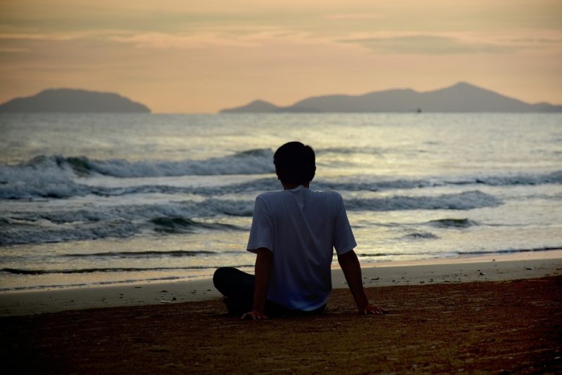 ung man i vit skjorta som sitter ensam på stranden