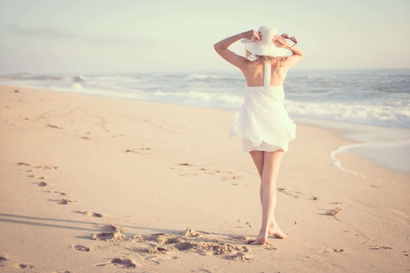 kvinna som bär den vita klänningen som går på stranden