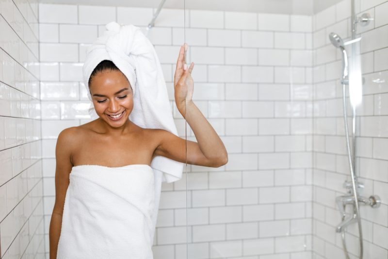 Ung kvinna i vita handdukar som slås in runt huvudet och kroppen efter dusch
