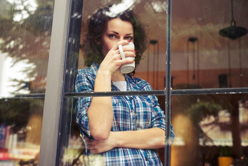 kvinna som dricker kaffe som står vid fönstret
