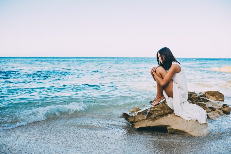 vacker flicka sitter på en klippa på stranden havet