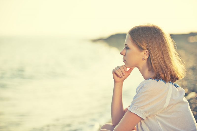 ledsen tjej som sitter vid kusten på stranden