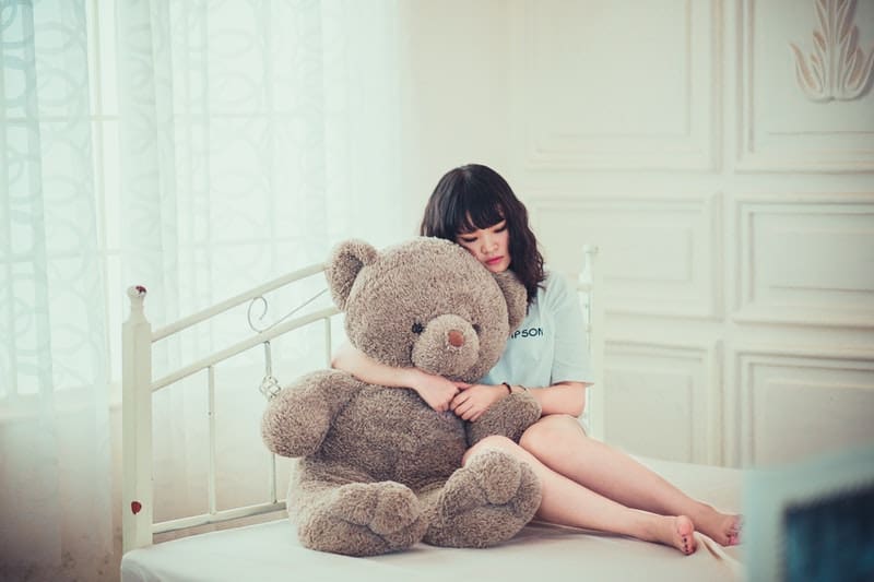 sorglig kvinna som kramar björnleksak i sängen