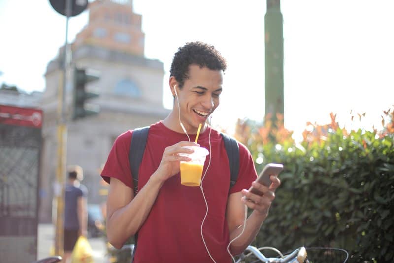 glad man med smarttelefonen som dricker juice på gatan