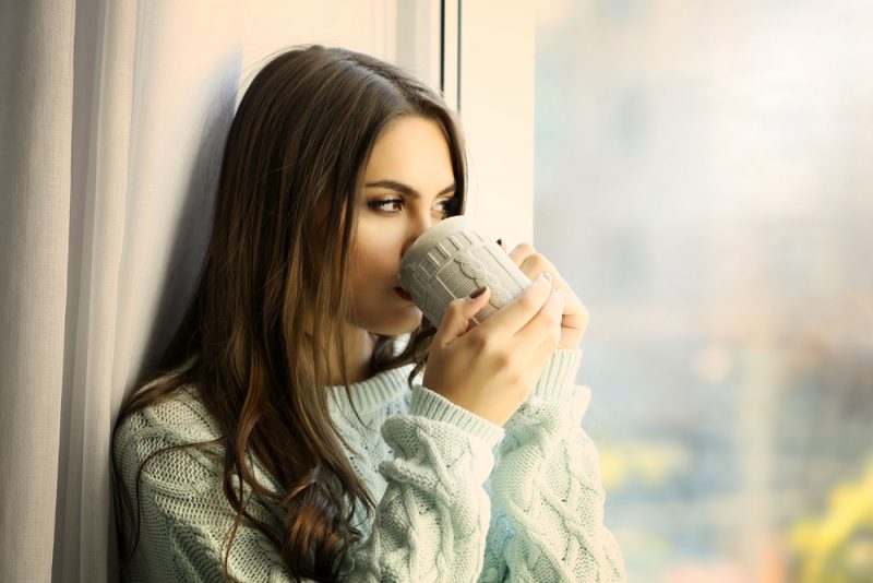 kvinna som dricker kaffe och sitter vid fönstret