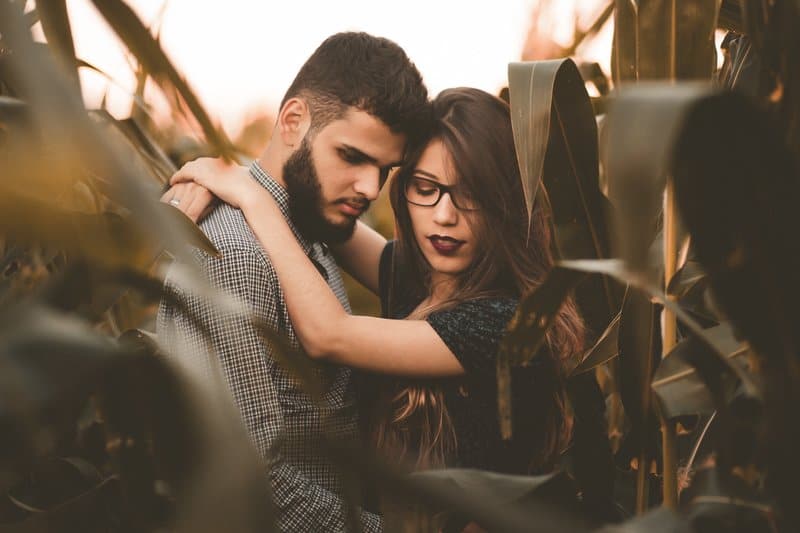 en man med skägg och en tjej med glasögon står omfamna i ett sädesfält