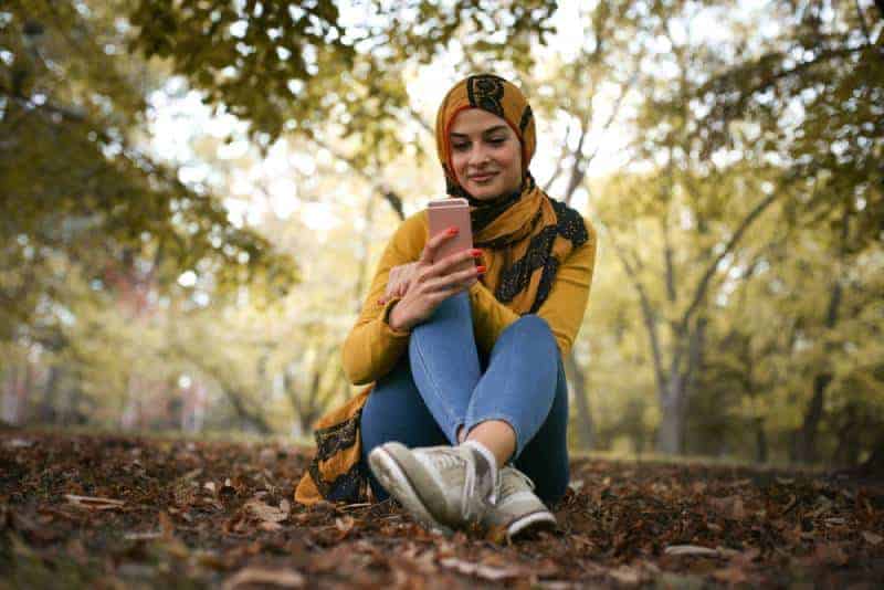 glad ung kvinna sitter i skogen och skriva på telefon
