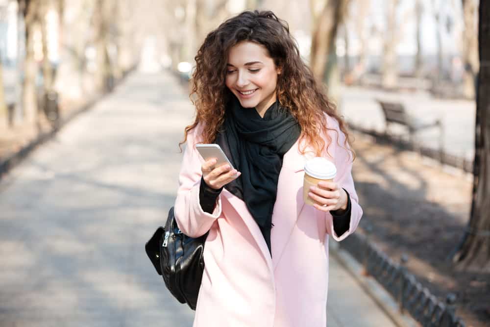 kvinna med rosa kappa leende medan du håller sin telefon