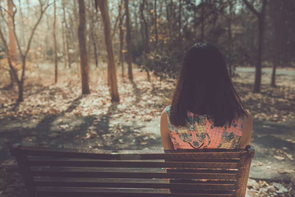 kvinna sitter på bänken i skogen