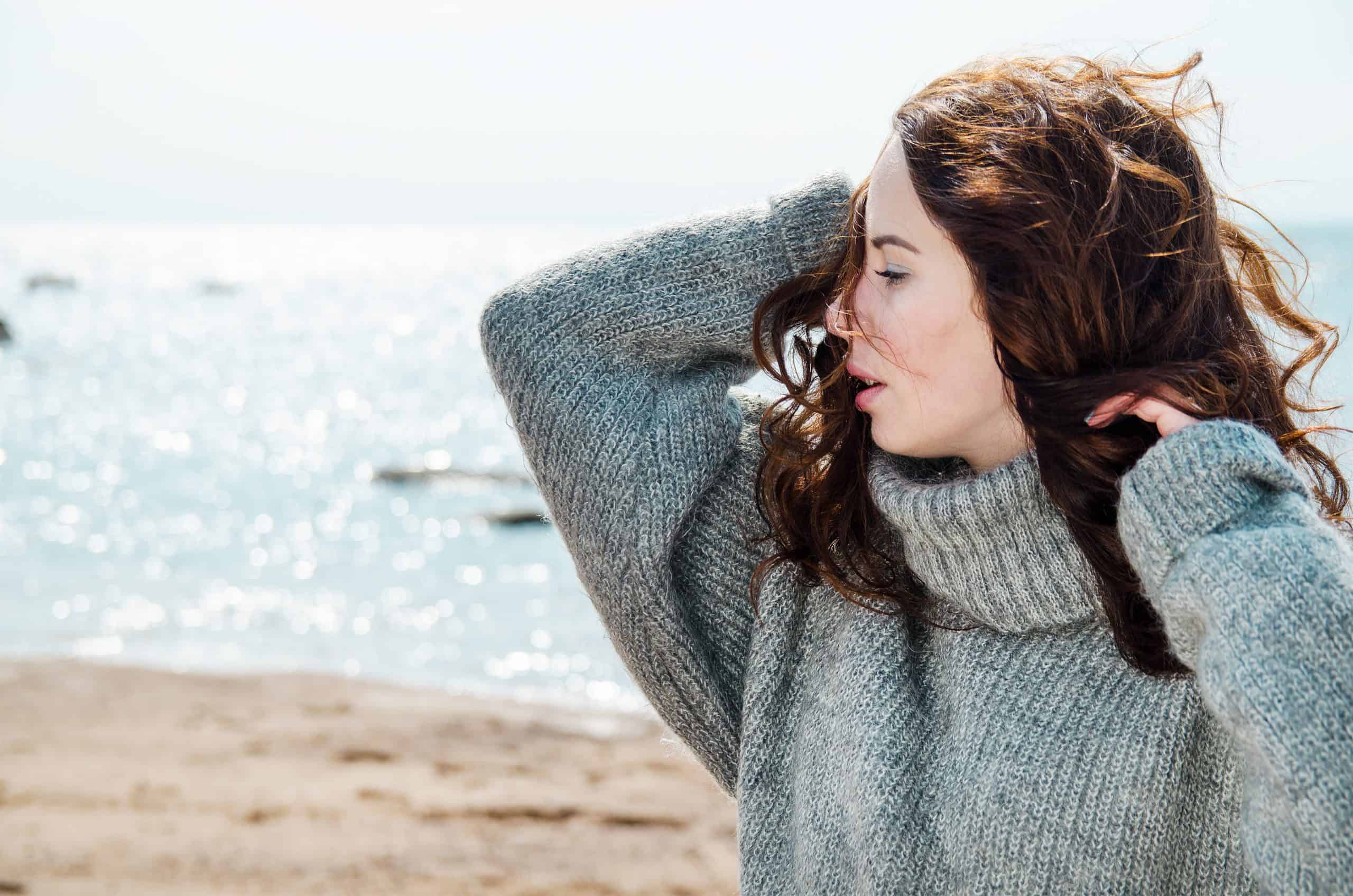 Attraktiv kvinna som bär en varm kofta på den kalla stranden