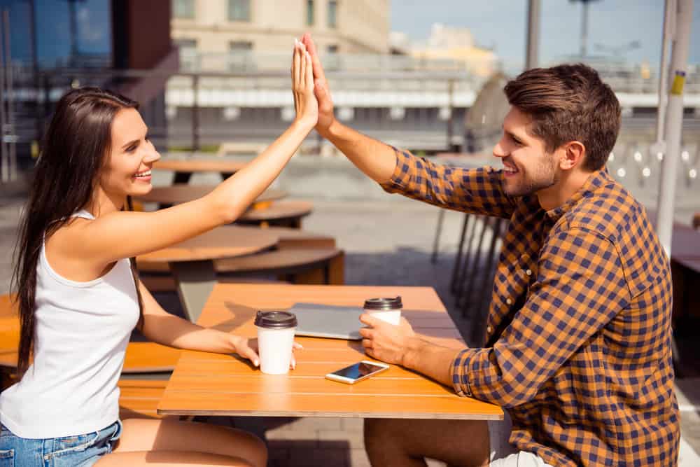 Lycklig vacker kvinna som ger hög fem till sin pojkvän i café