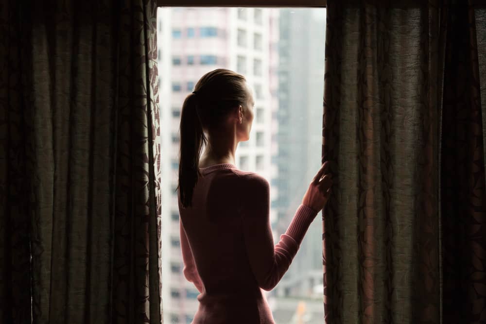 Ung kvinna som ser ut hennes lägenhetfönster