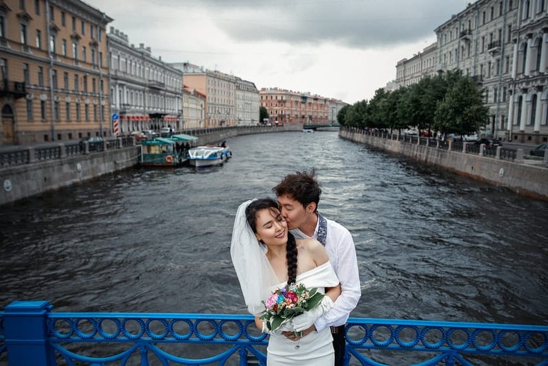 brudgummen och bruden i ett omfamning på bron med det blå staketet