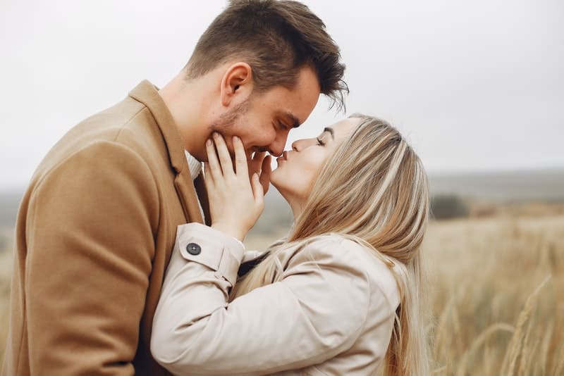 en flicka i en grå kappa i ett gräsfält kysser sin man på näsan