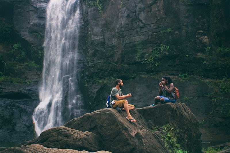 en man och en kvinna sitter på en klippa nära ett vattenfall