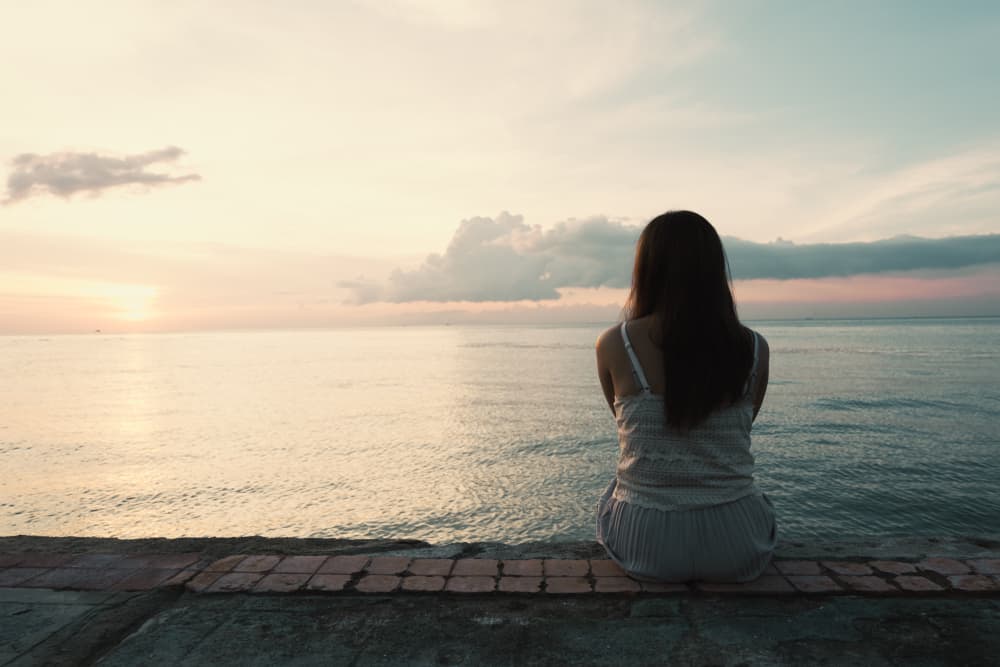 kvinna sitter nära havet i solnedgången