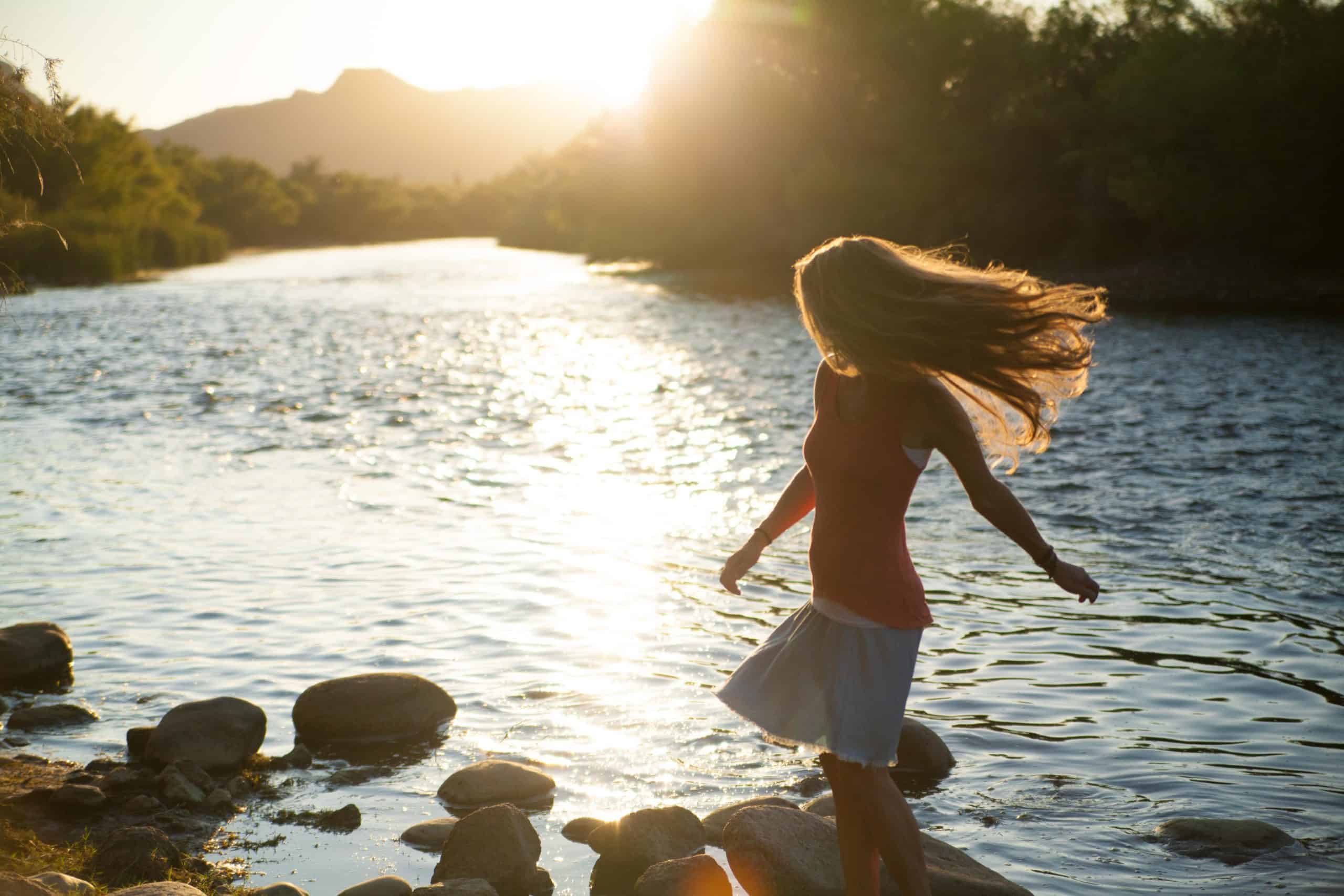 kvinna som går nära floden i solnedgången med hår som flyger i vinden