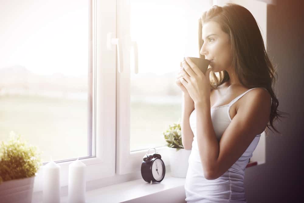 kvinna tittar genom fönstret och tar en slurk kaffe