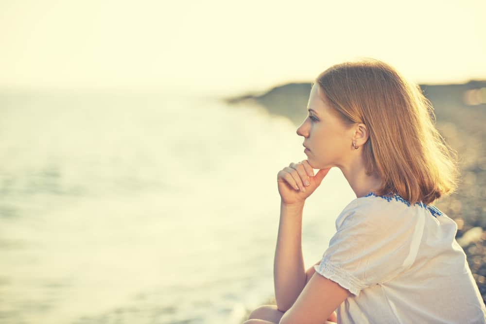 ledsen tjej som sitter vid kusten på stranden och tittar på avståndet till havs