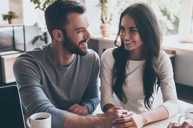 leende par som tittar på varandra på café
