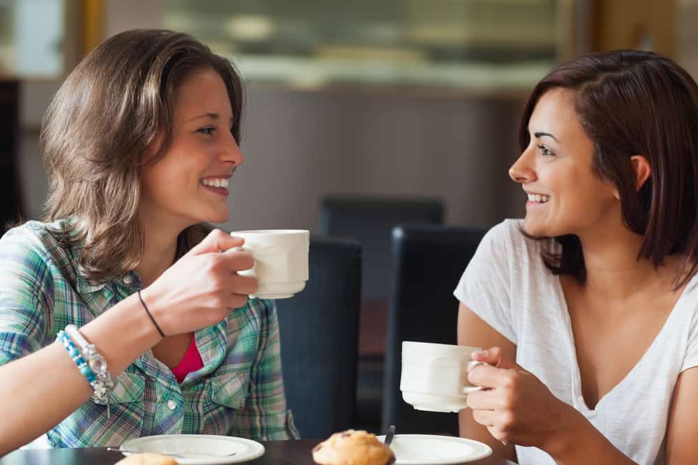 två kvinnliga vänner som dricker kaffe och äter kakor