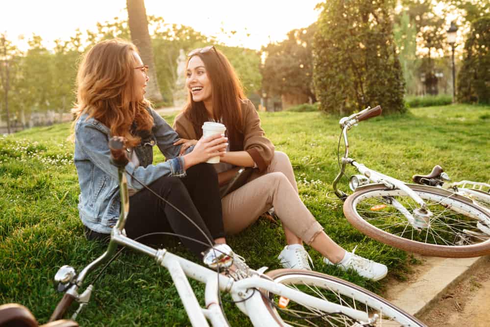 två unga vackra kvinnavänner utomhus med cyklar i park