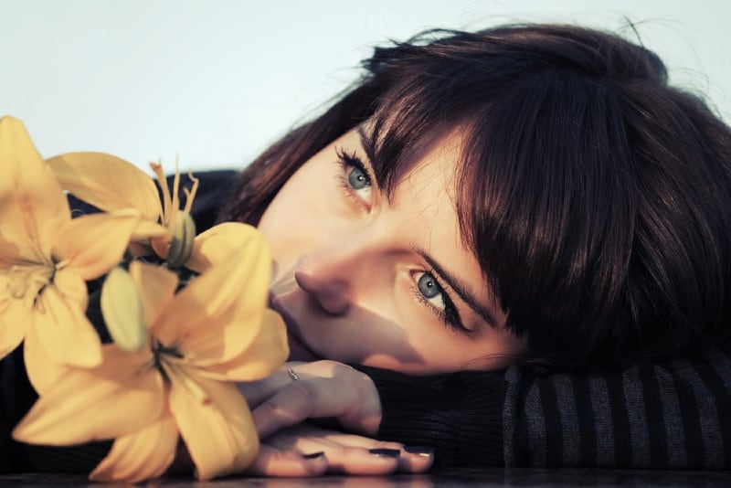 Porträtt av en sorglig vacker kvinna med gula blommor