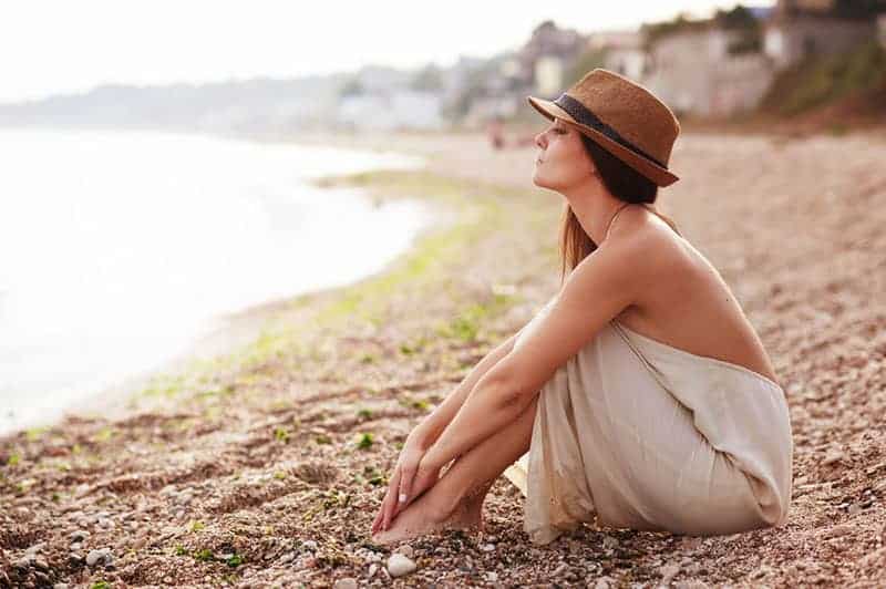 ung kvinna med hatt sitter på stranden
