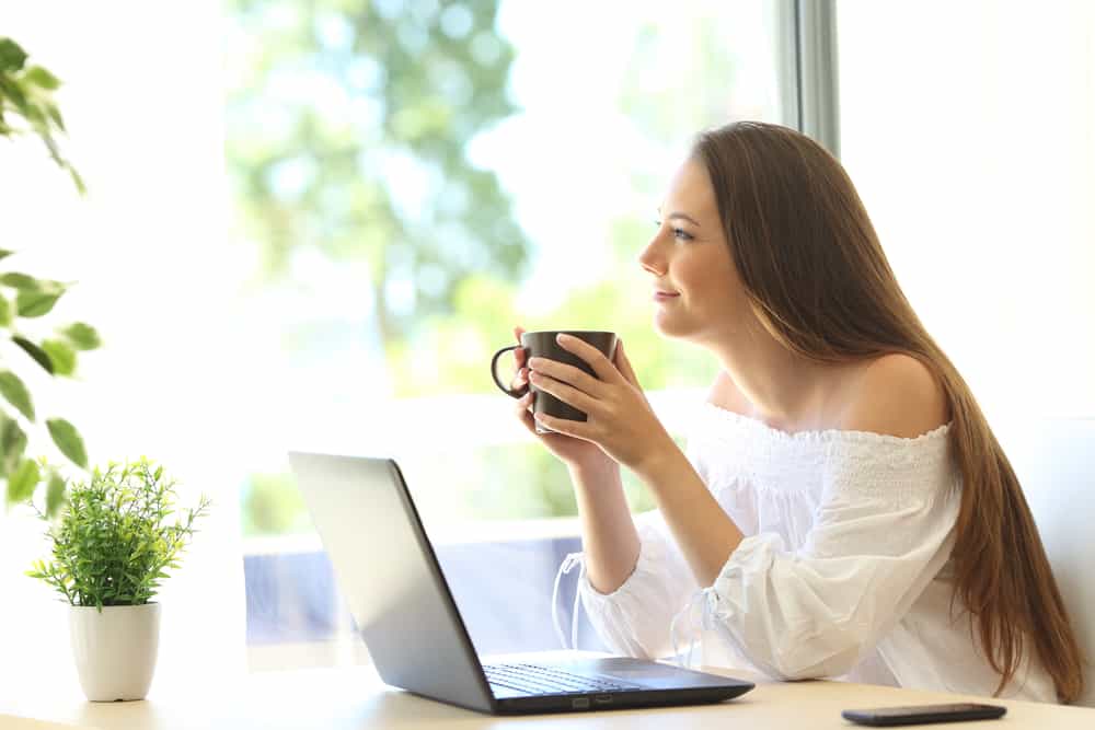 ung lycklig kvinna som håller kaffe och arbetar