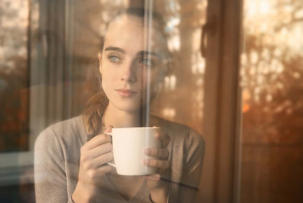 vacker kvinna dricker kaffe på morgonen sitter vid fönstret