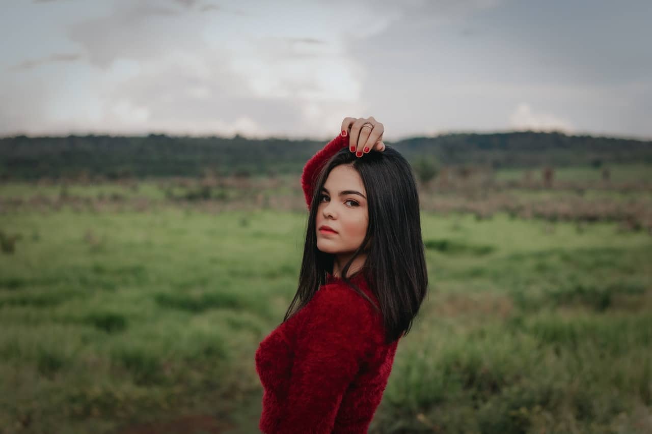 Kvinna i röd tröja som står ensam på posera för grönt gräsfält