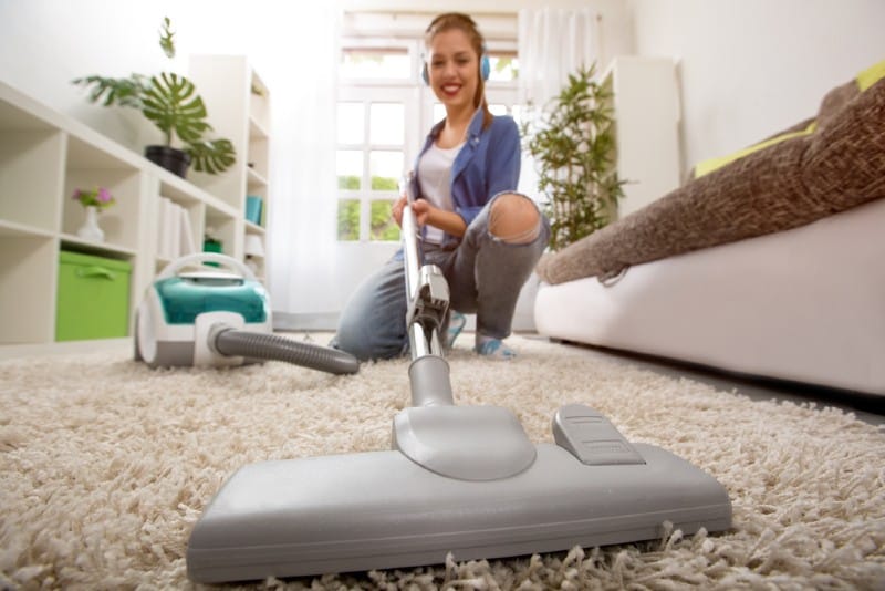 Kvinna med dammsugare som gör ren mattan hemma