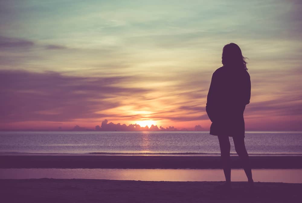 Ung kvinna som står på stranden i havet och ser till soluppgång