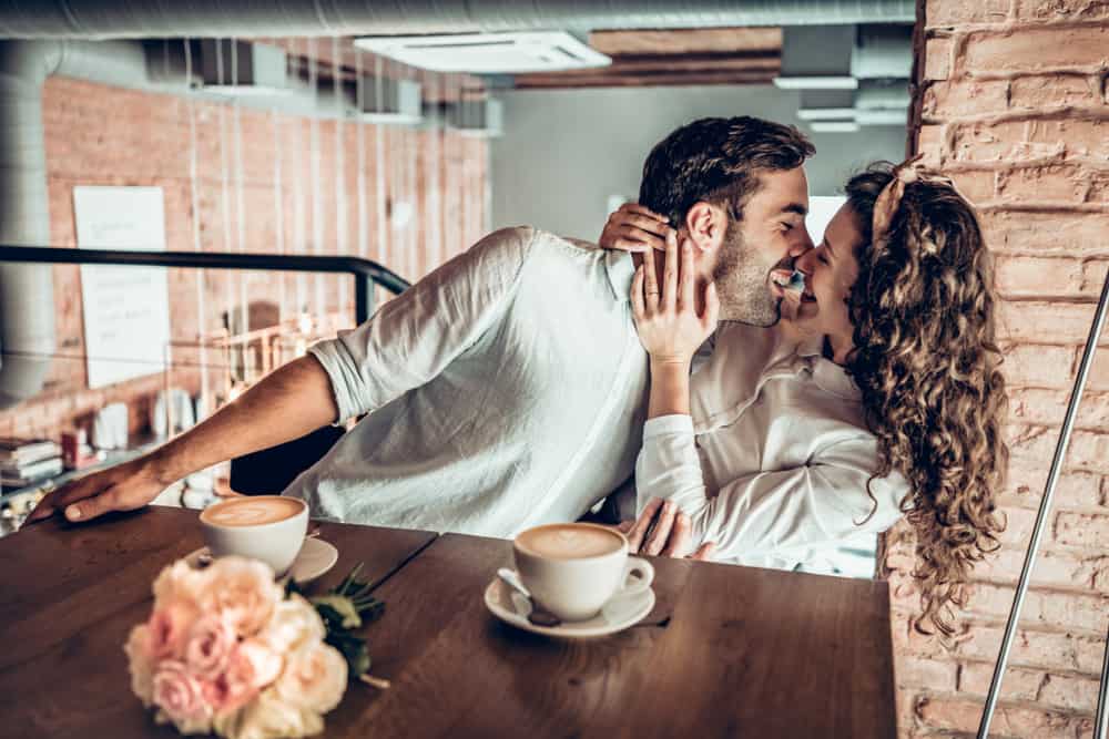 Vackra romantiska par som kyssas lekfullt medan de sitter i kafé