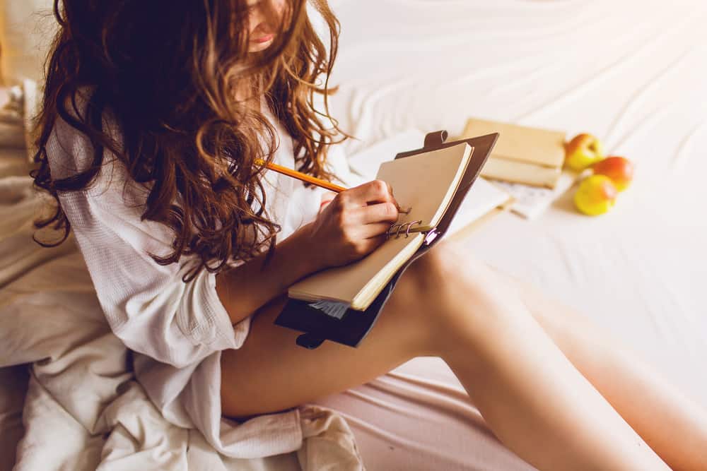 bild av ganska ung kvinna som sitter på sin mysiga säng och gör anteckningar