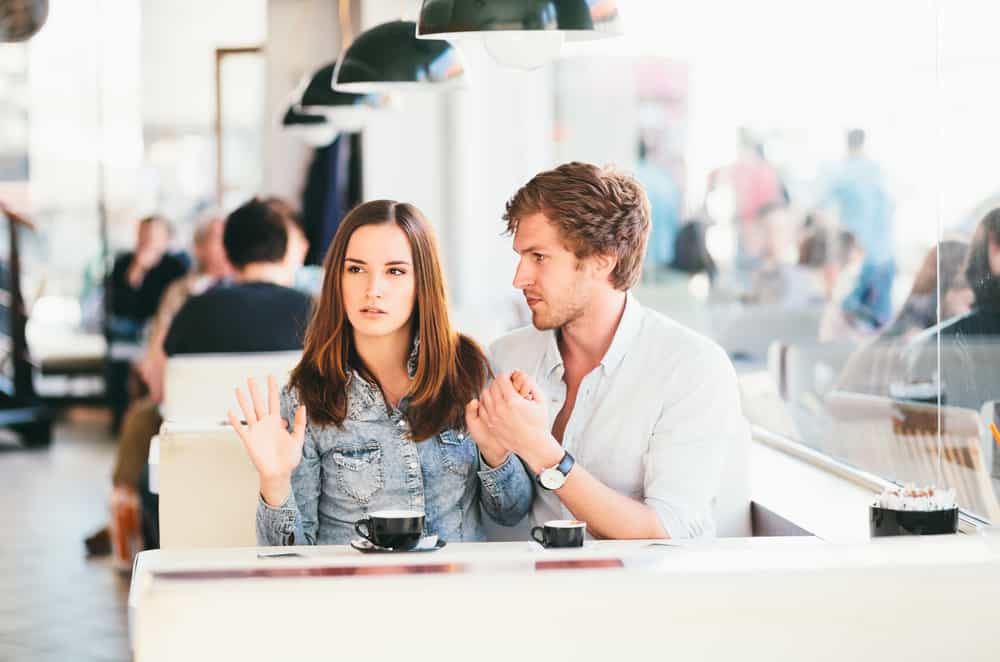 en arg kvinna i en denimskjorta sitter på ett café med en sorglig man