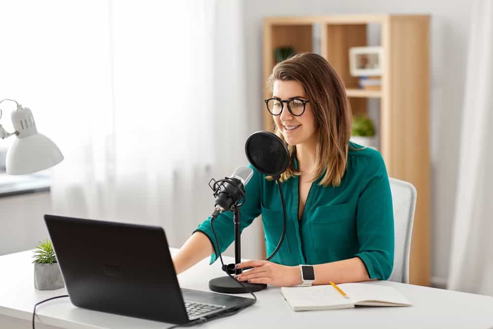 en glad kvinna i en grön t-shirt använder en bärbar dator och en professionell mikrofon