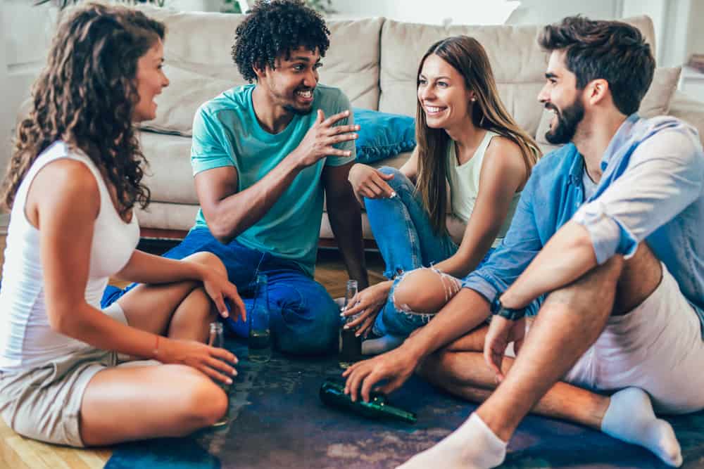 en grupp vänner med en öl sitter på golvet och spelar ett spel med sanning eller utmaning