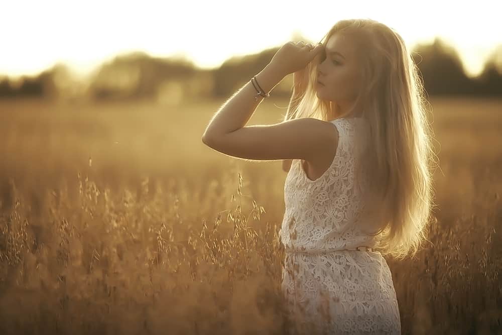 en kvinna i en vit klänning står i ett vetefält