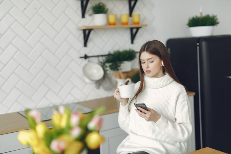en kvinna i en vit rulle sitter och använder en mobiltelefon med te