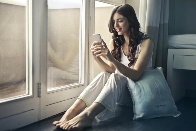 en kvinna i kärlek i en nattklänning sitter vid fönstret och skriver en sms