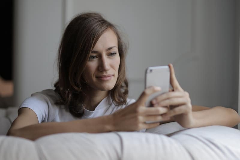 en kvinna i kärlek i sängen skriver ett meddelande på sin mobiltelefon