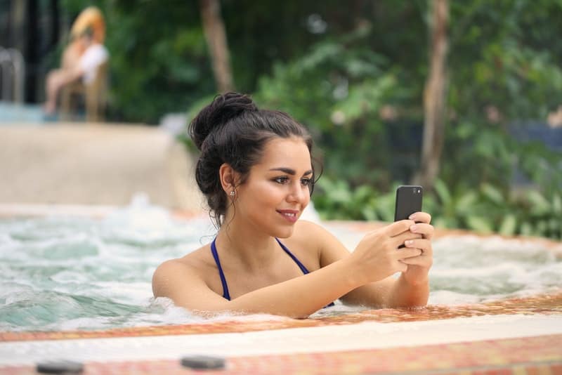en kvinna i poolen använder en smartphone