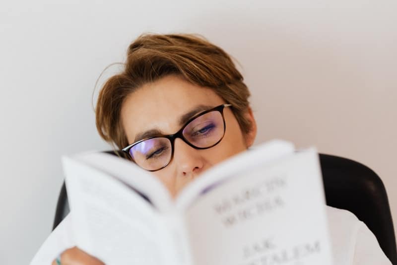 en kvinna med glasögon sitter och läser en bok