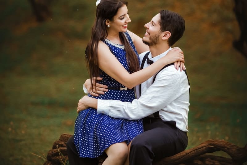 en le kvinna i en blå prickklänning sitter i knäet på hennes man i naturen
