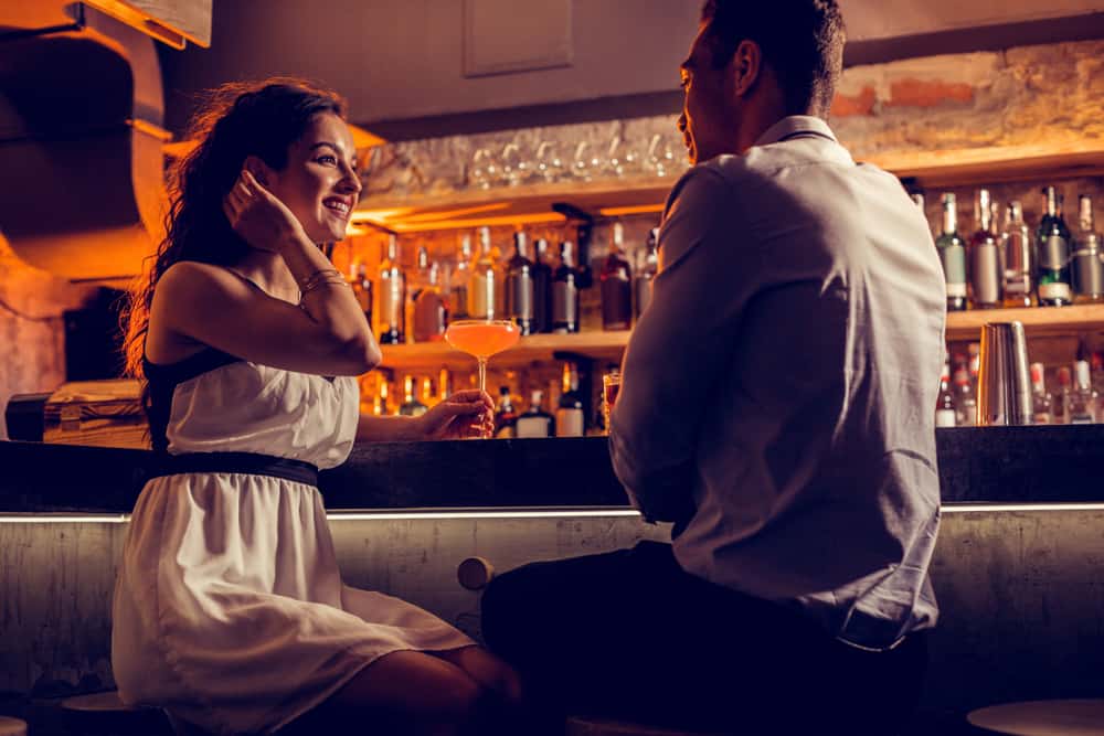 en leende kvinna och en man i en vit skjorta flirta i baren
